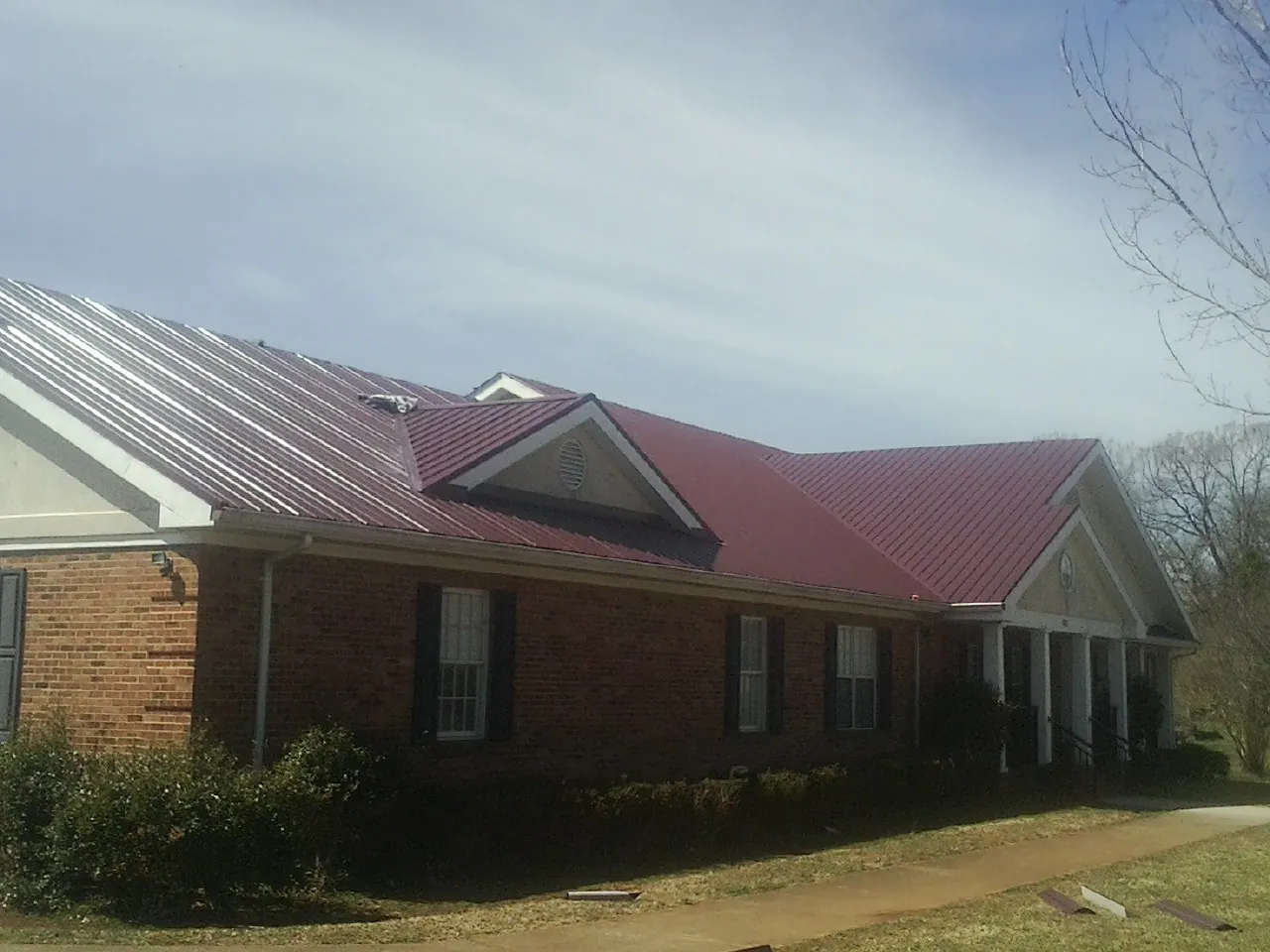 Red metal roof with gabled entries on a long brick building, from a Hail Damage Roof Repair job in Flemington