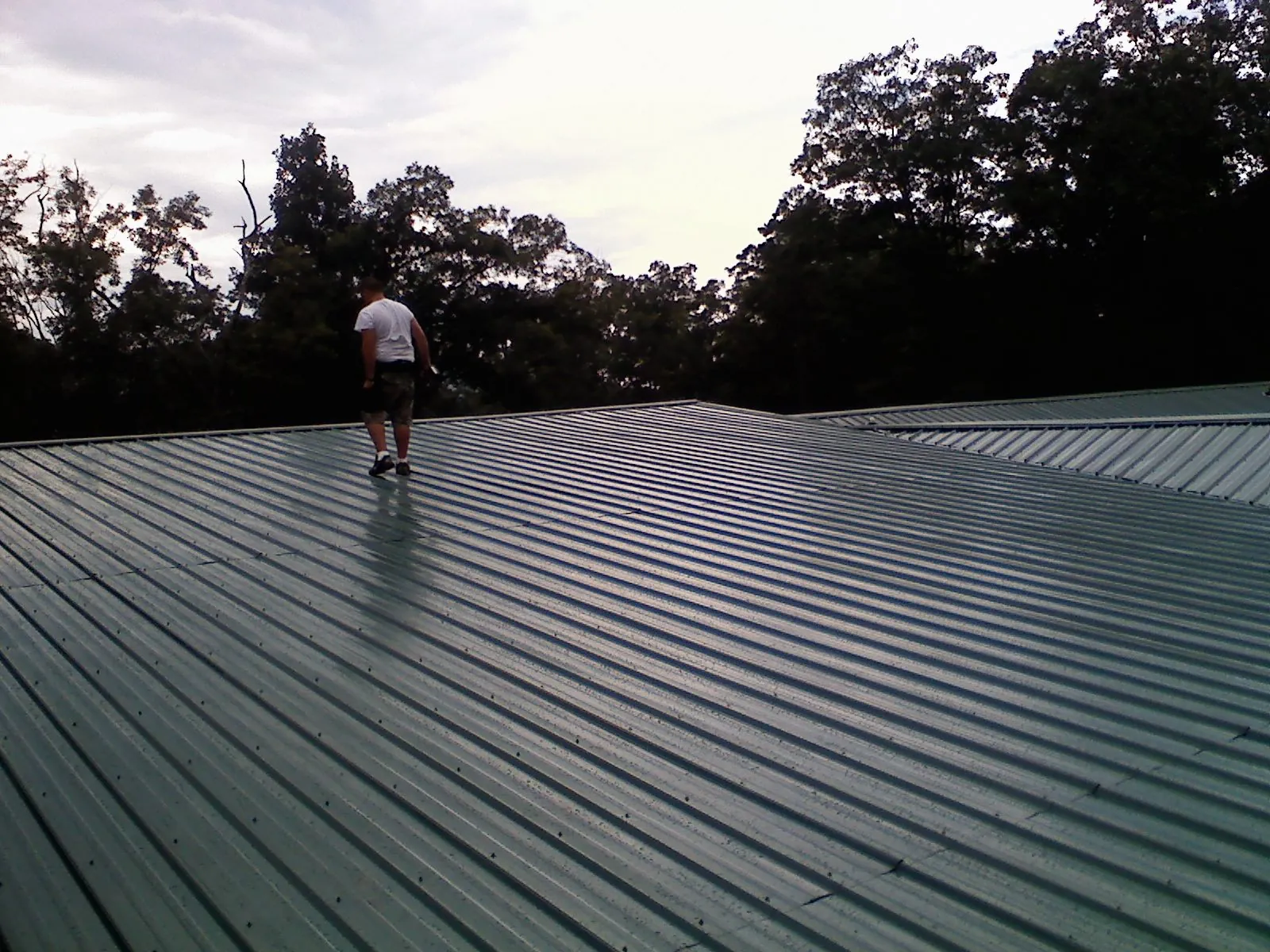 Roofer walking a wide expanse of new green metal roofing in Flemington