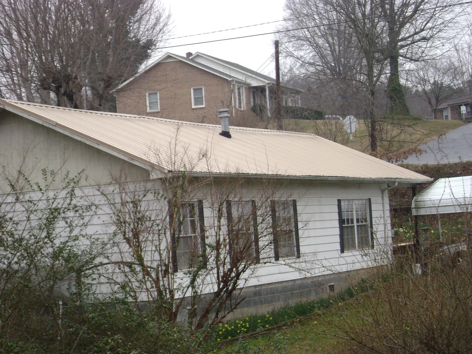 Tan metal roof on a white sided house set into a hillside — Commercial Roofing by Roofing Brothers in Flemington